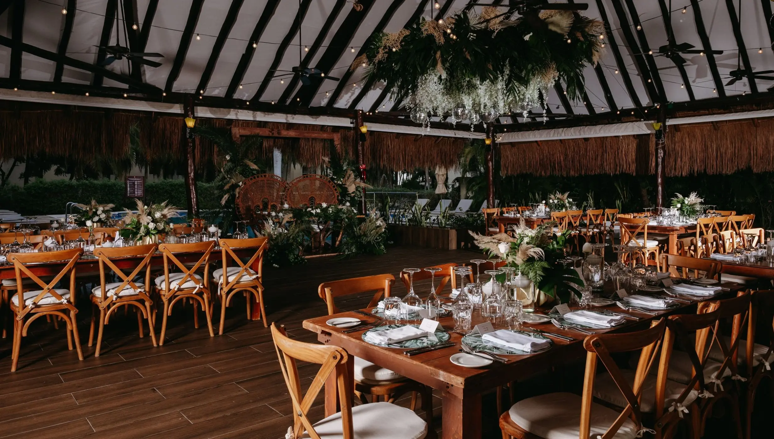 Indoor wedding reception under a palapa with wooden cross-back chairs at El Dorado Royale, Riviera Maya