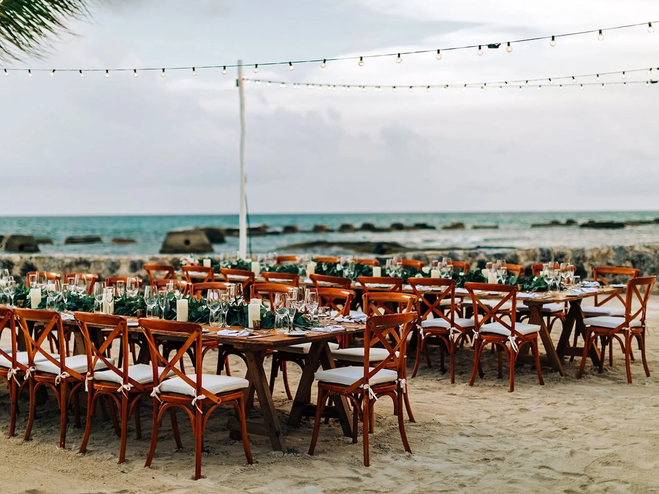 Beachfront wedding reception setup with wooden tables and string lights at El Dorado Royale, Riviera Maya