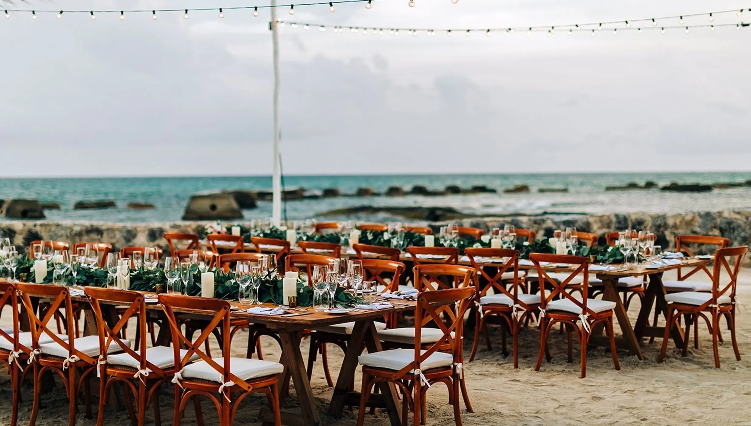 Beachfront wedding reception setup with wooden tables and string lights at El Dorado Royale, Riviera Maya