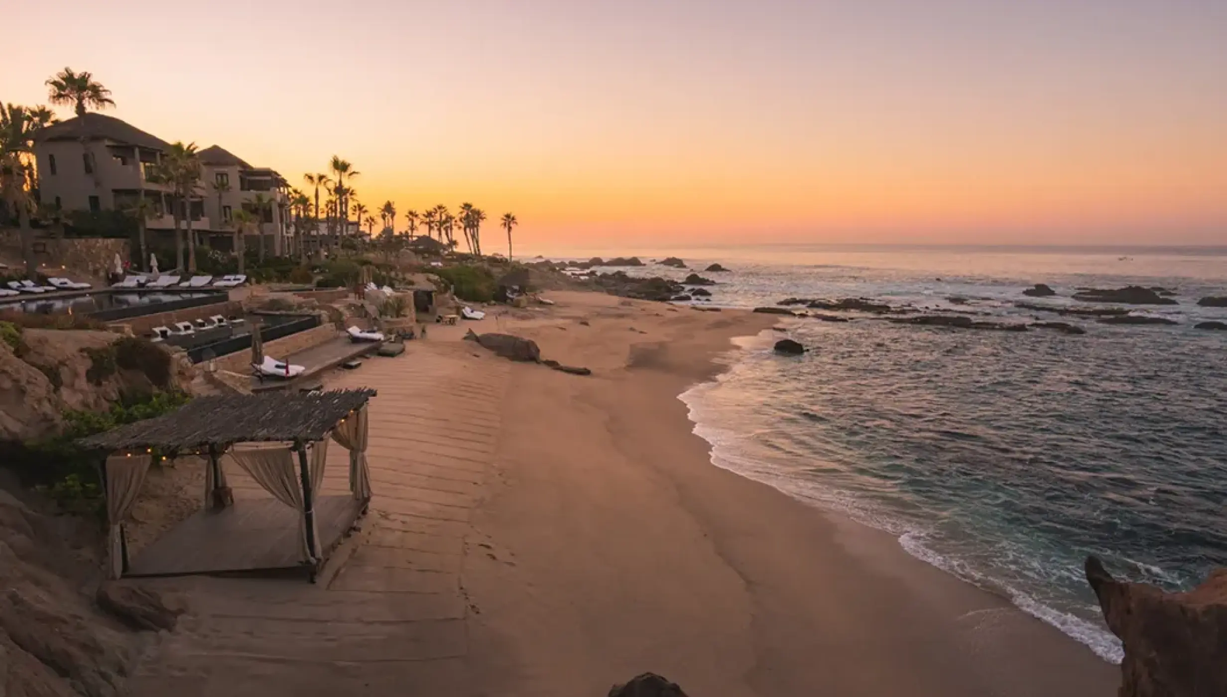 Private beach with a palapa and rocky shoreline at sunset at Esperanza Cabo San Lucas