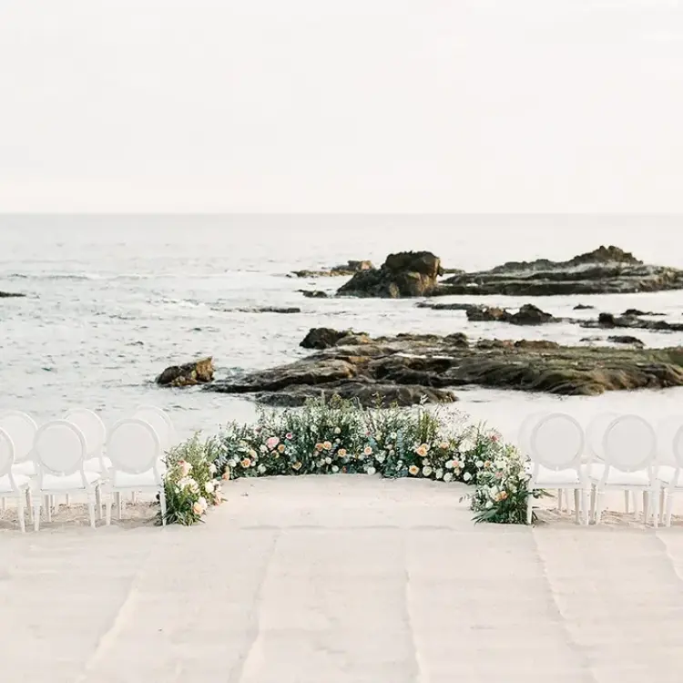 Beachfront wedding ceremony with white chairs and floral arch at Esperanza Cabo San Lucas