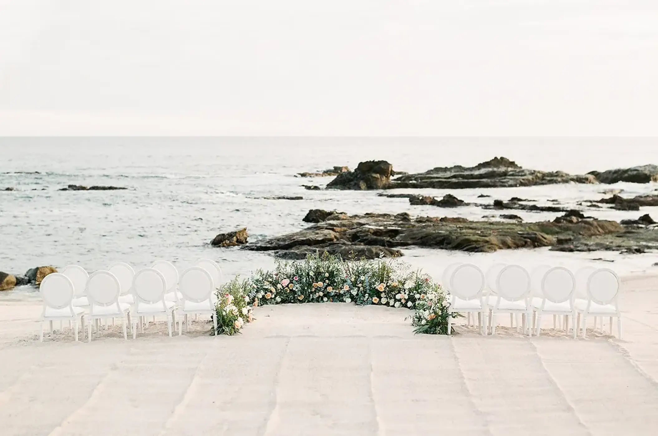 Beachfront wedding ceremony with white chairs and floral arch at Esperanza Cabo San Lucas