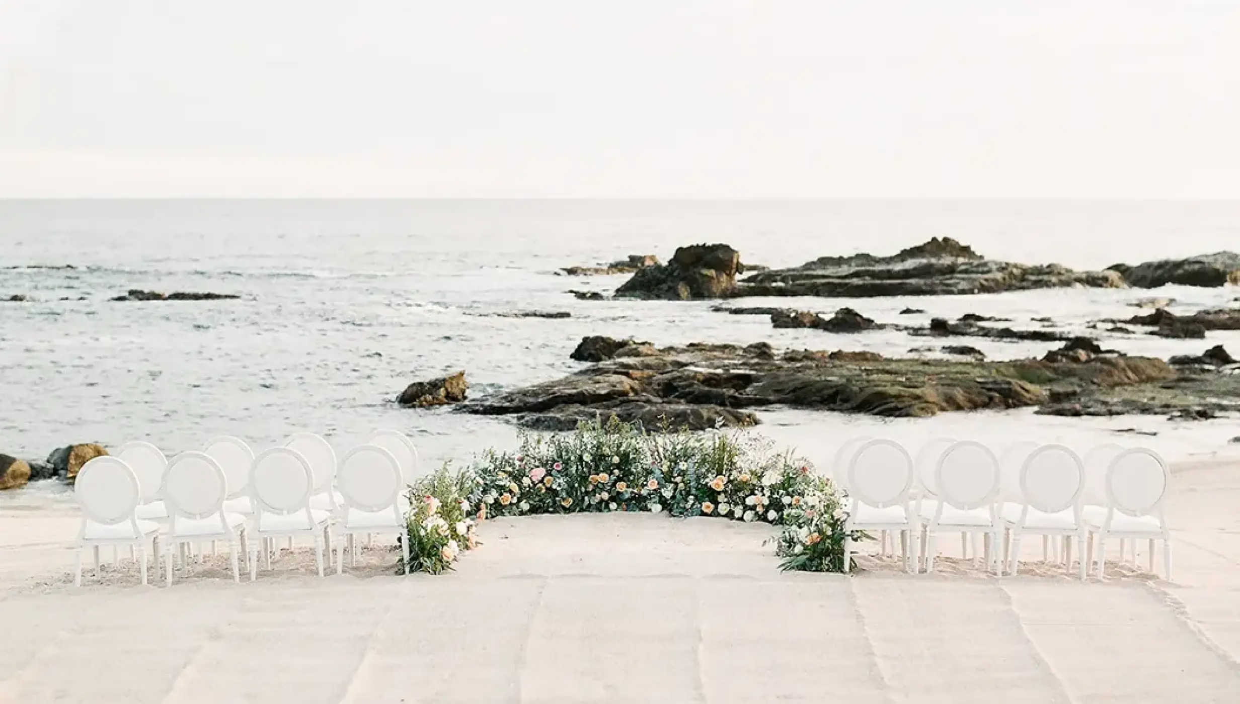 Beachfront wedding ceremony with white chairs and floral arch at Esperanza Cabo San Lucas