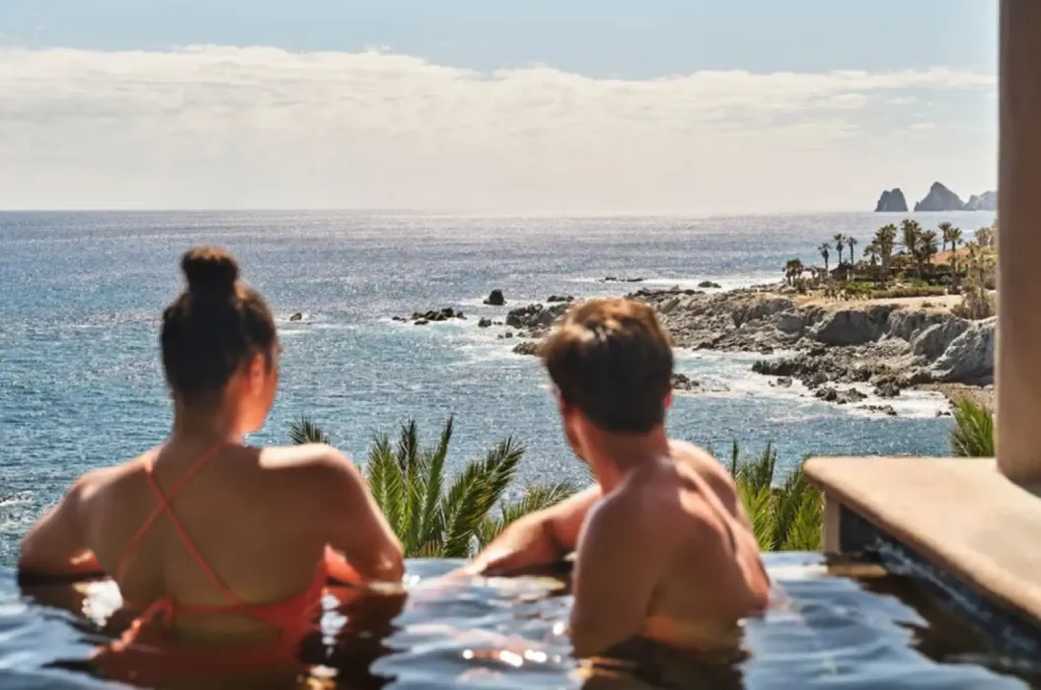 Couple in an infinity pool overlooking the rocky coastline at Esperanza, Cabo San Lucas