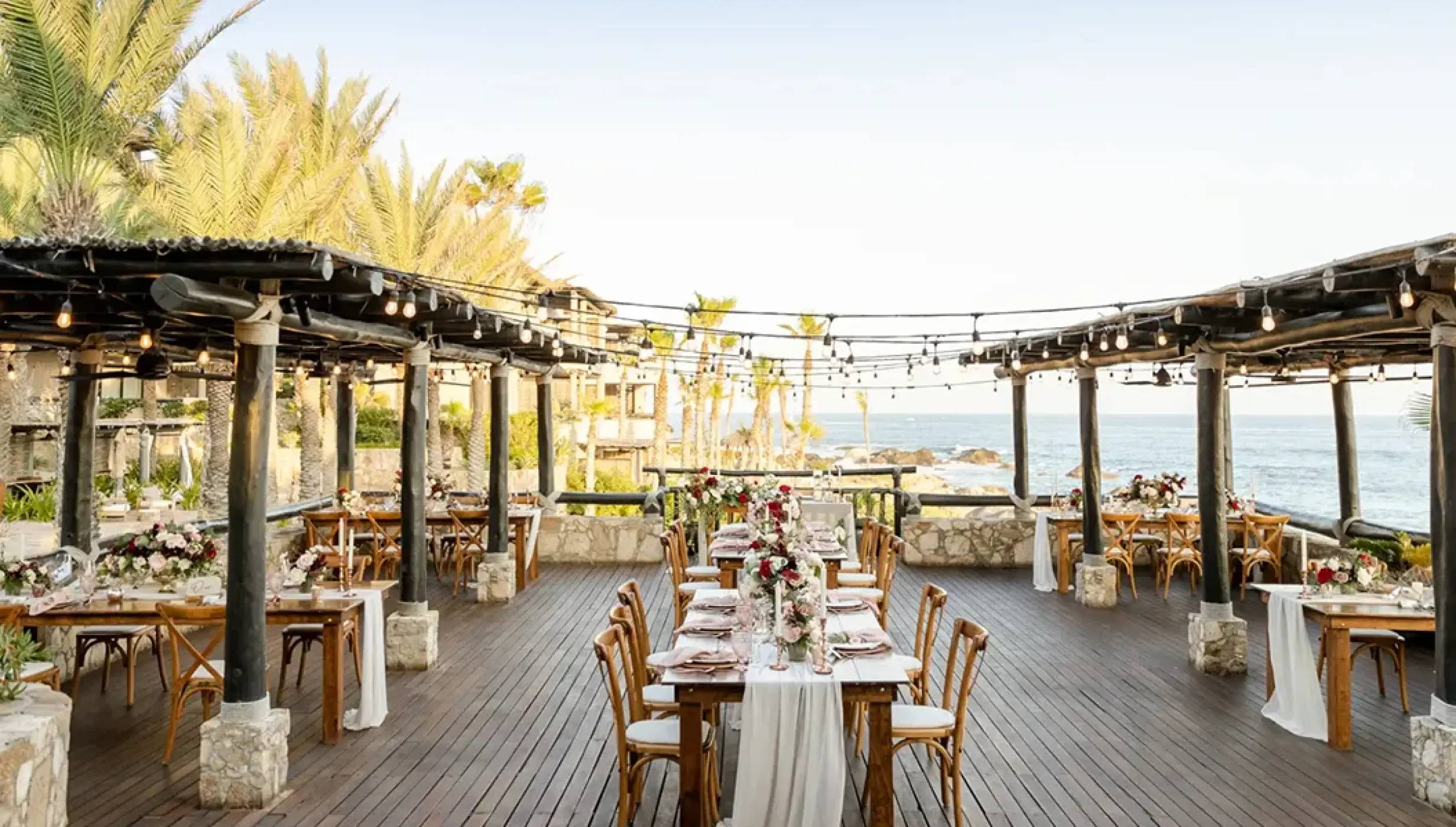 Oceanfront wedding reception with wooden tables and string lights at Esperanza, Cabo San Lucas