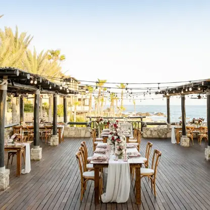 Oceanfront wedding reception with wooden tables and string lights at Esperanza, Cabo San Lucas