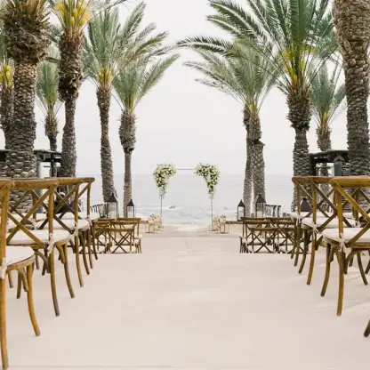 Wedding ceremony setup with wooden cross-back chairs and palm trees at Esperanza, Cabo San Lucas