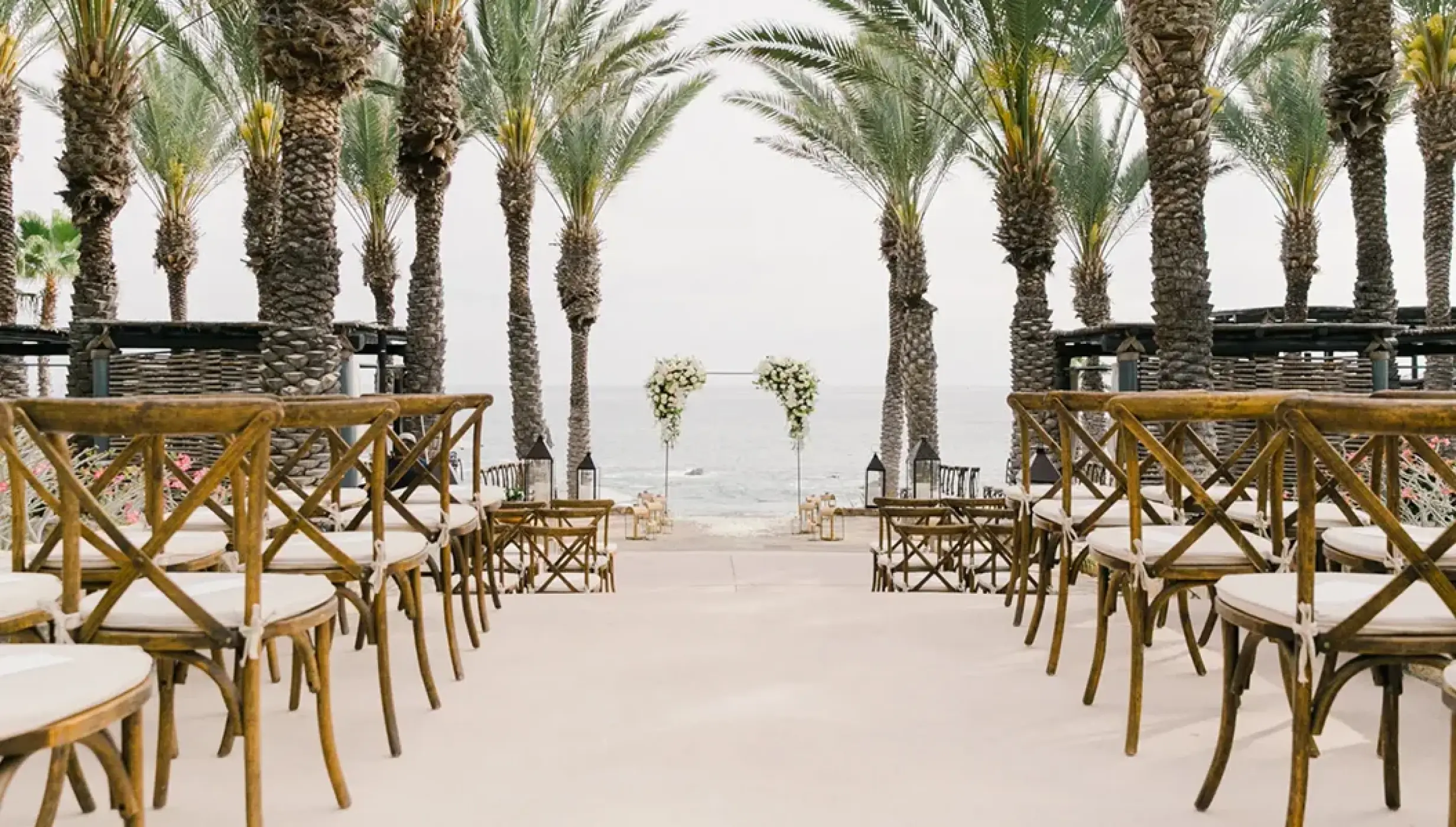 Wedding ceremony setup with wooden cross-back chairs and palm trees at Esperanza, Cabo San Lucas