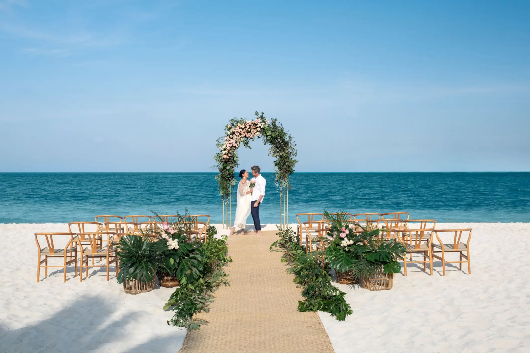 Beachfront wedding ceremony with a floral arch and wooden chairs at Excellence Coral Playa Mujeres, Cancun
