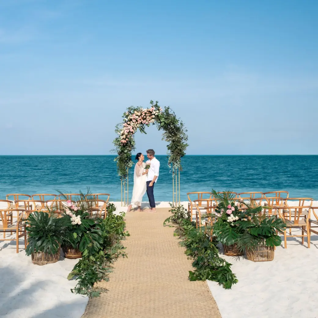 Beachfront wedding ceremony with a floral arch and wooden chairs at Excellence Coral Playa Mujeres, Cancun