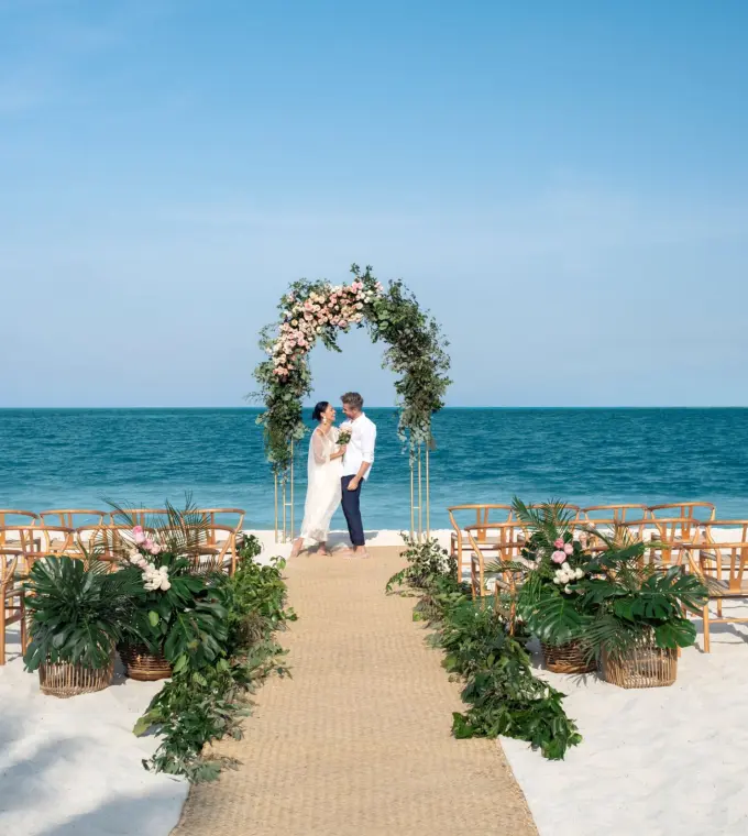 Beachfront wedding ceremony with a floral arch and wooden chairs at Excellence Coral Playa Mujeres, Cancun