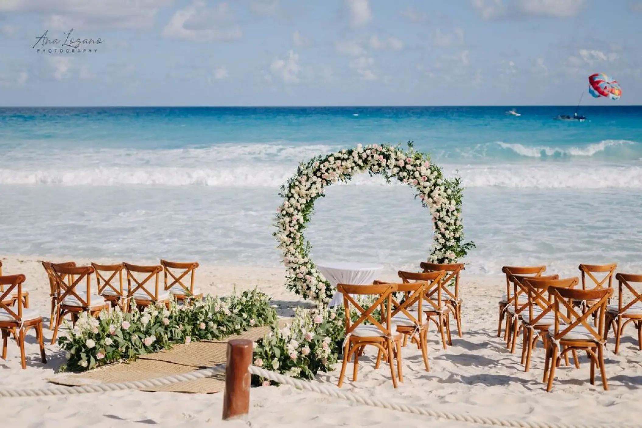 Beach wedding ceremony with a circular floral arch and wooden chairs at Fiesta Americana Condesa, Cancun