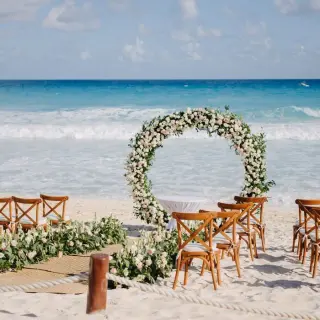 Beach wedding ceremony with a circular floral arch and wooden chairs at Fiesta Americana Condesa, Cancun