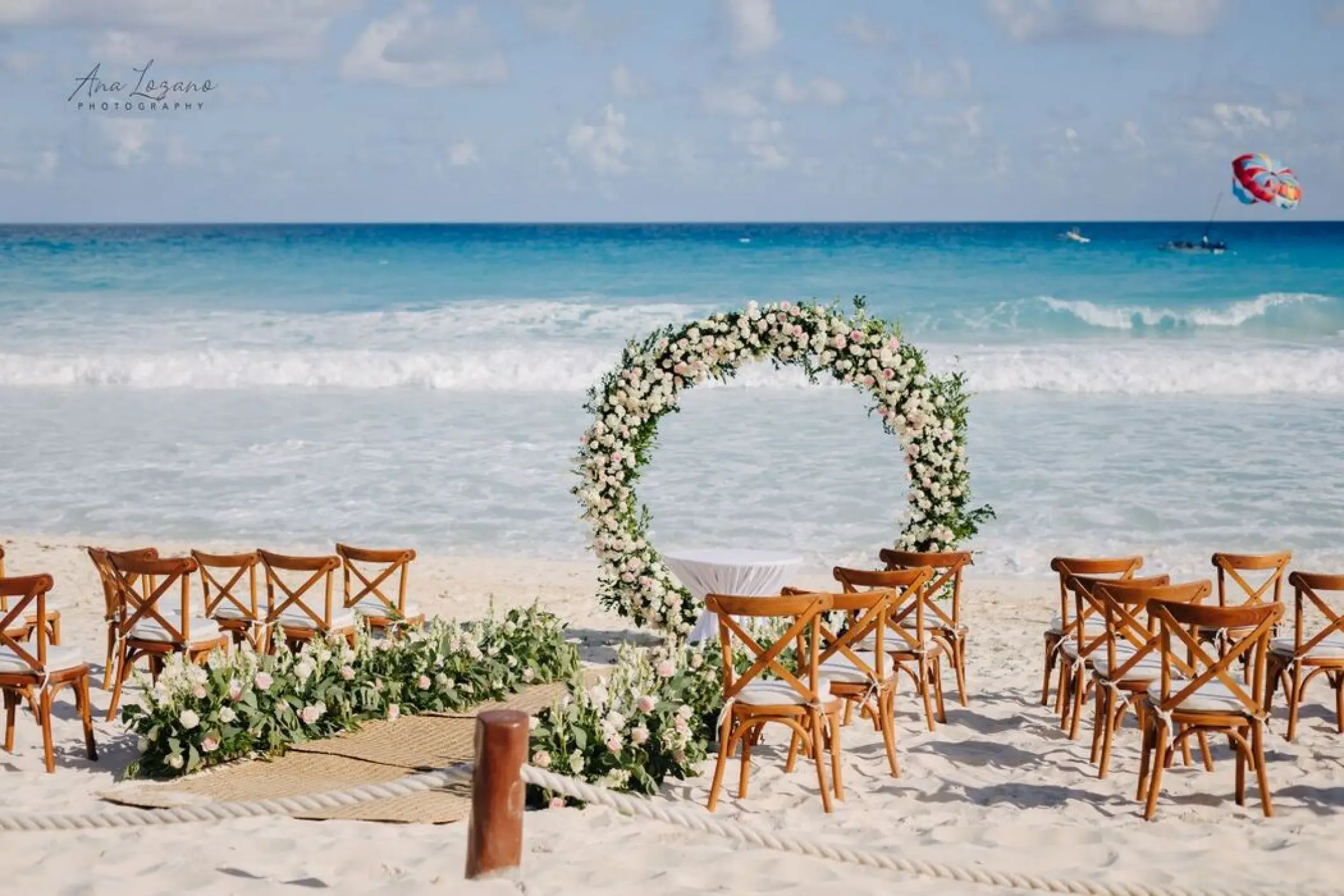 Beach wedding ceremony with a circular floral arch and wooden chairs at Fiesta Americana Condesa, Cancun