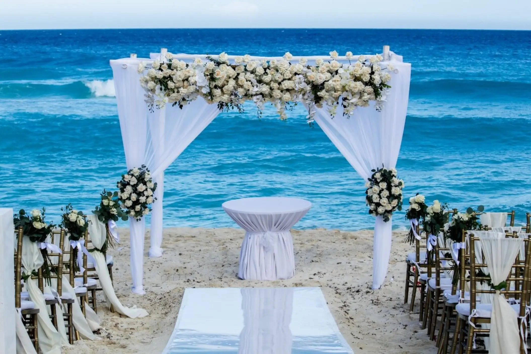 Beachfront wedding ceremony setup with white floral arch at Fiesta Americana Condesa, Cancun
