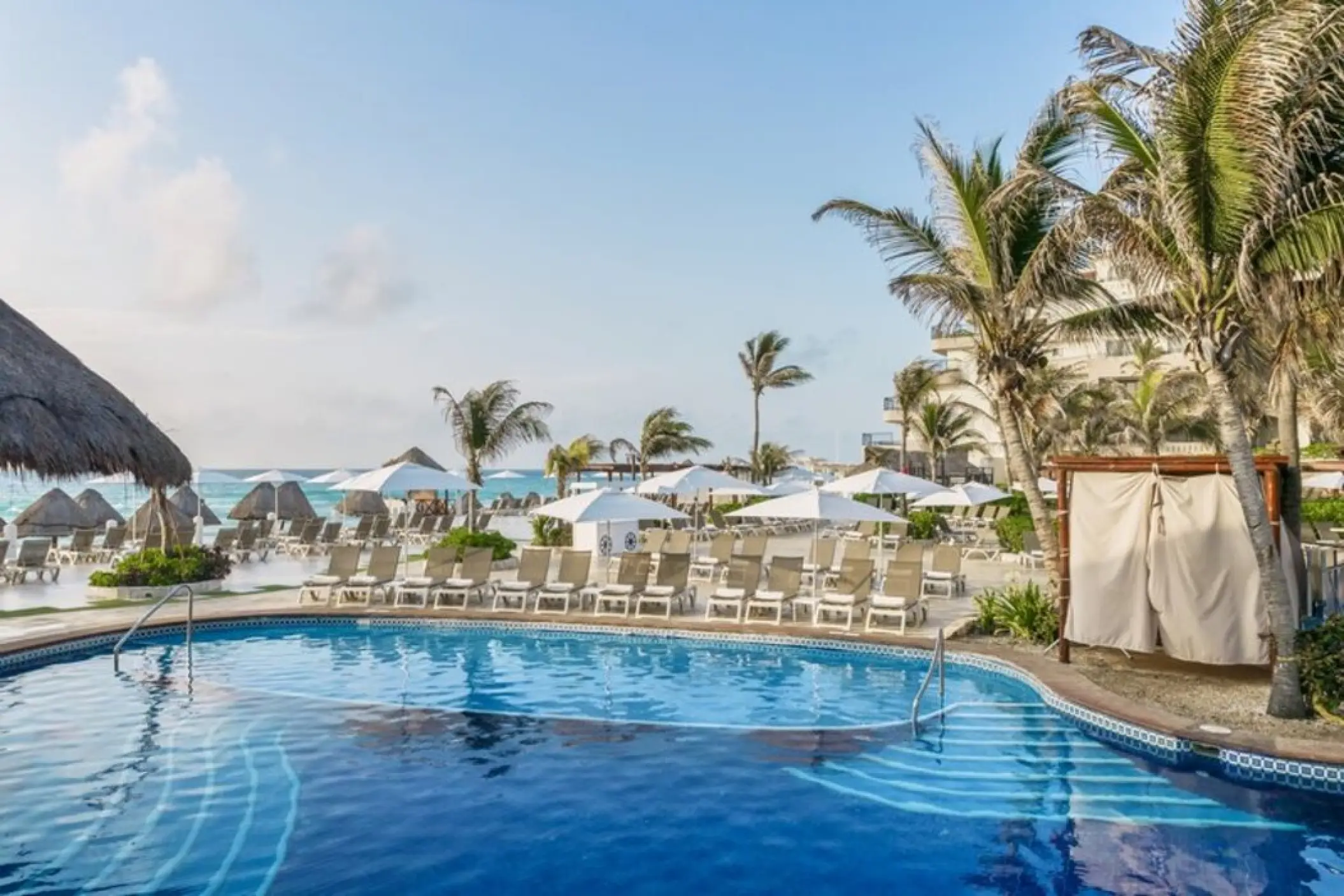 Outdoor swimming pool with loungers and palm trees at Fiesta Americana Condesa, Cancun