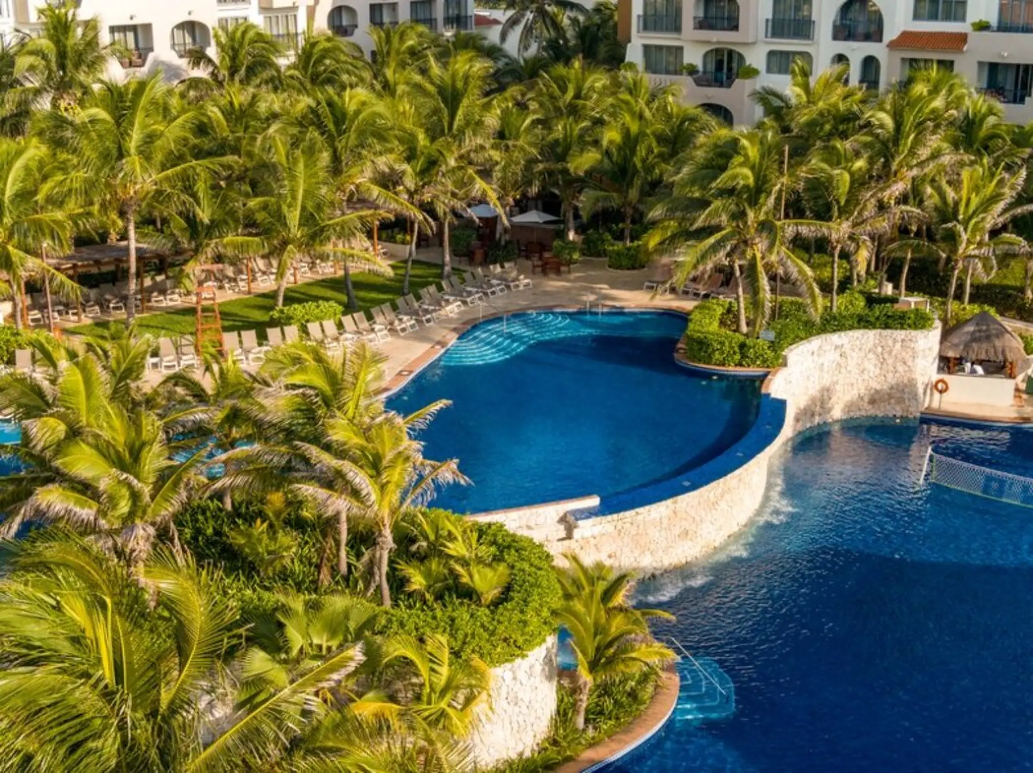 Tiered pool area with stone walls and palm trees at Fiesta Americana Condesa, Cancun