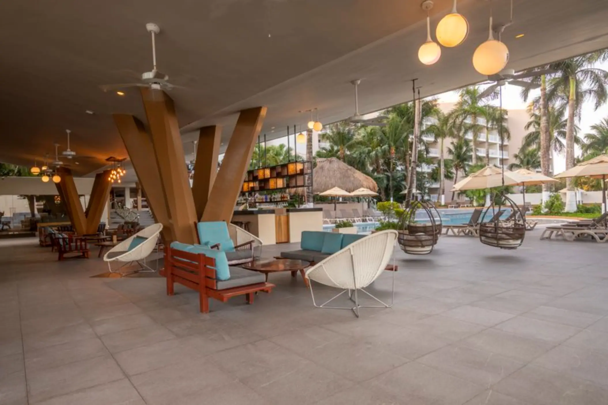 Open-air lobby bar with modern lounge seating and hanging chairs at Fiesta Americana Cozumel