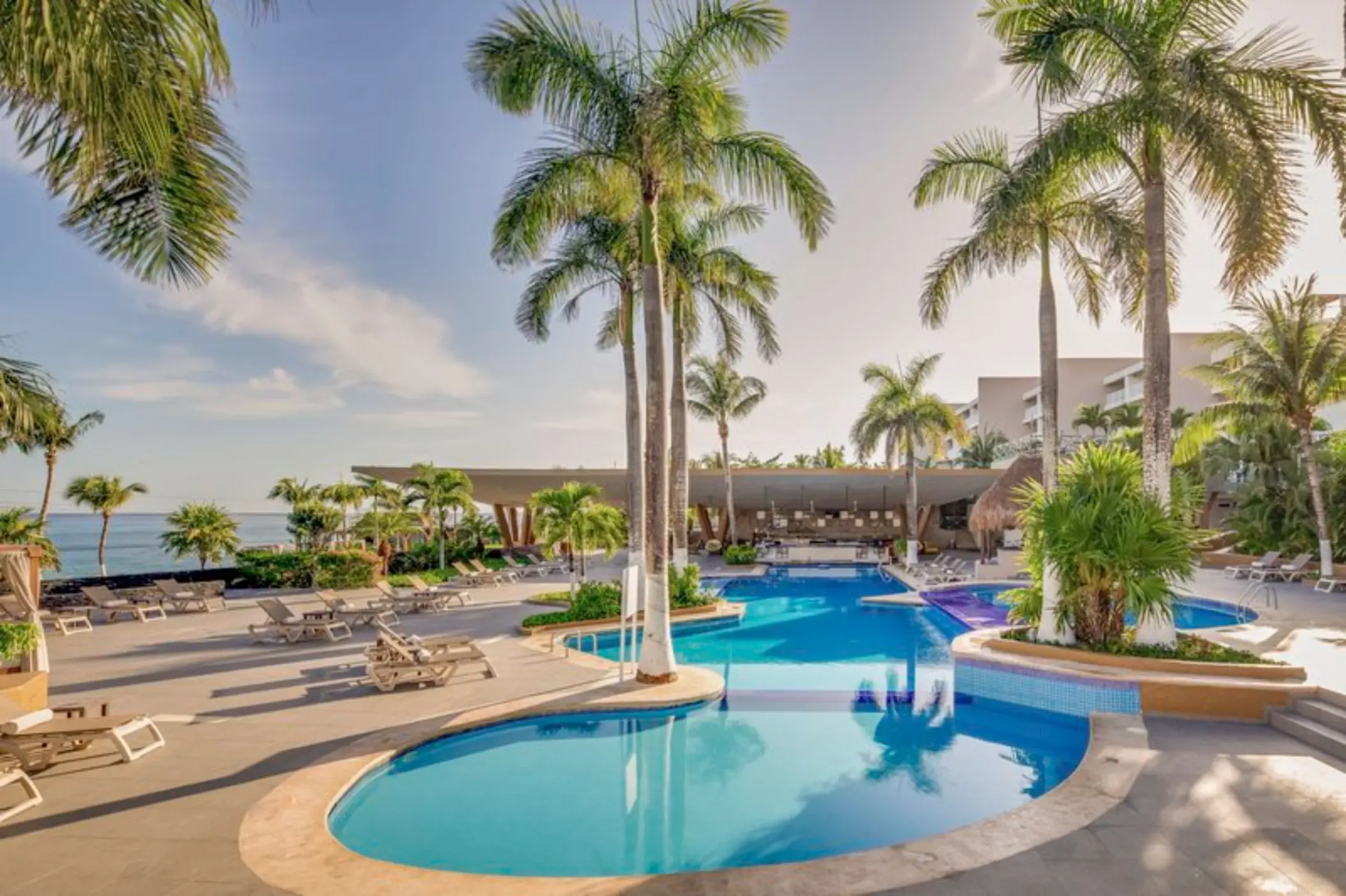Outdoor swimming pool and swim-up bar surrounded by palm trees at Fiesta Americana Cozumel