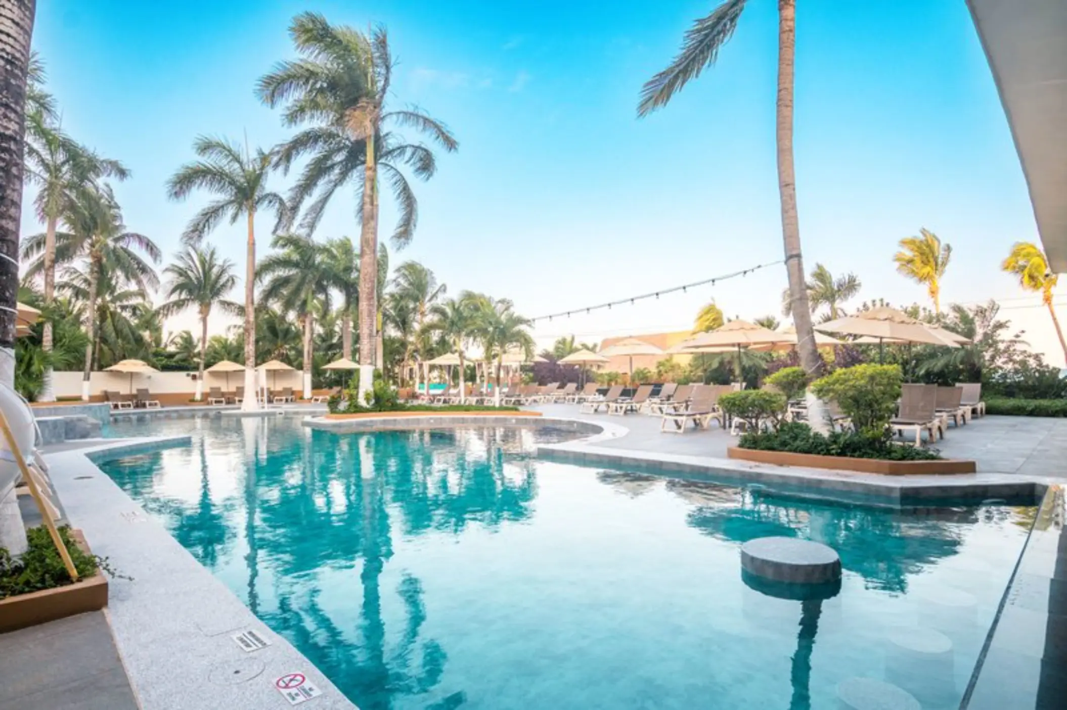 Main pool area with sun loungers and palm trees at Fiesta Americana Cozumel