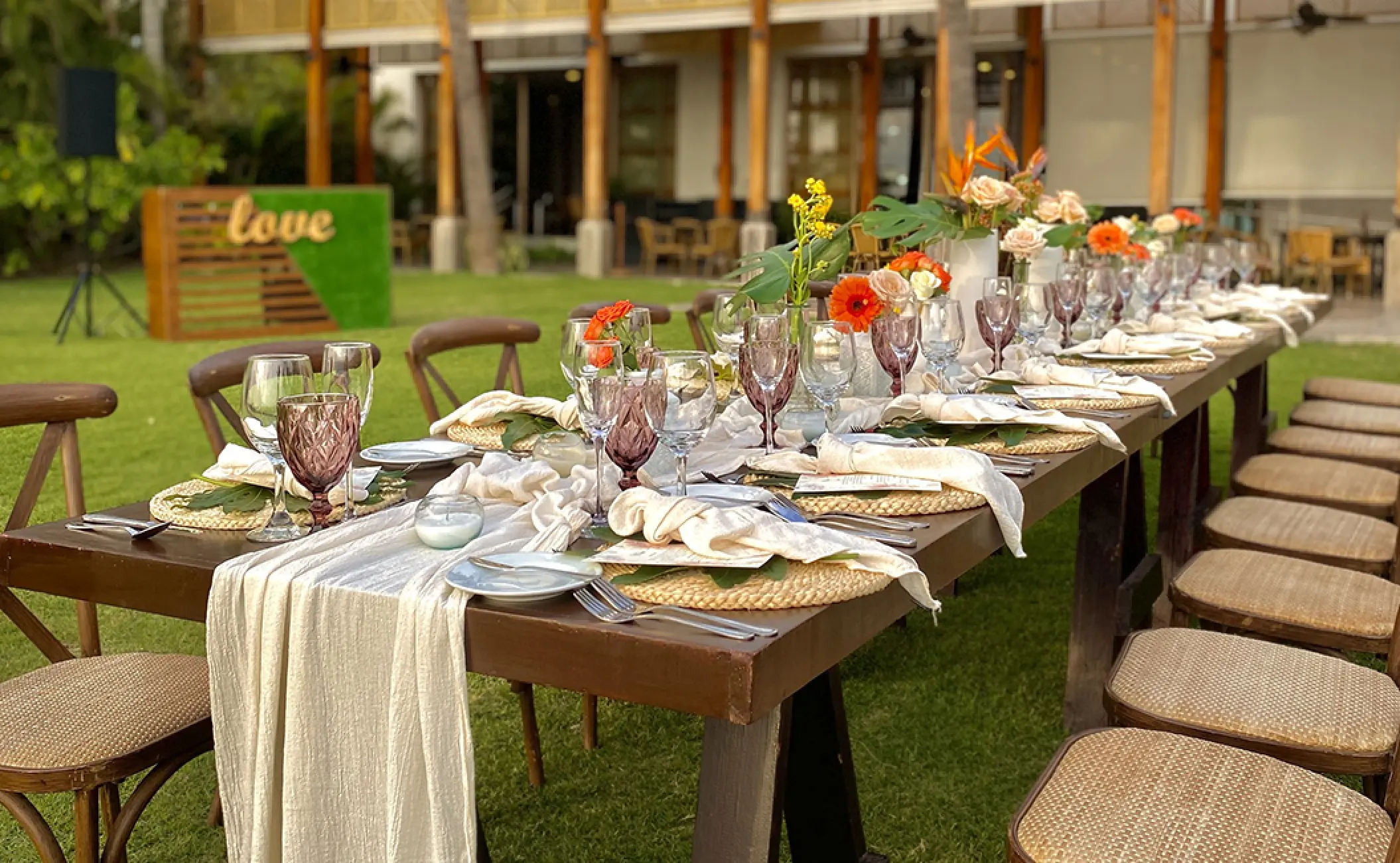 Outdoor wedding reception setup on a lawn with long wooden tables and floral runners at Fiesta Americana Puerto Vallarta