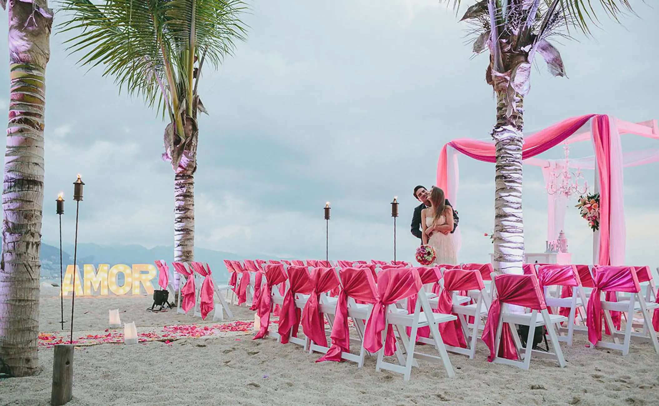 Beach wedding ceremony with pink decor and white chairs at Fiesta Americana Puerto Vallarta