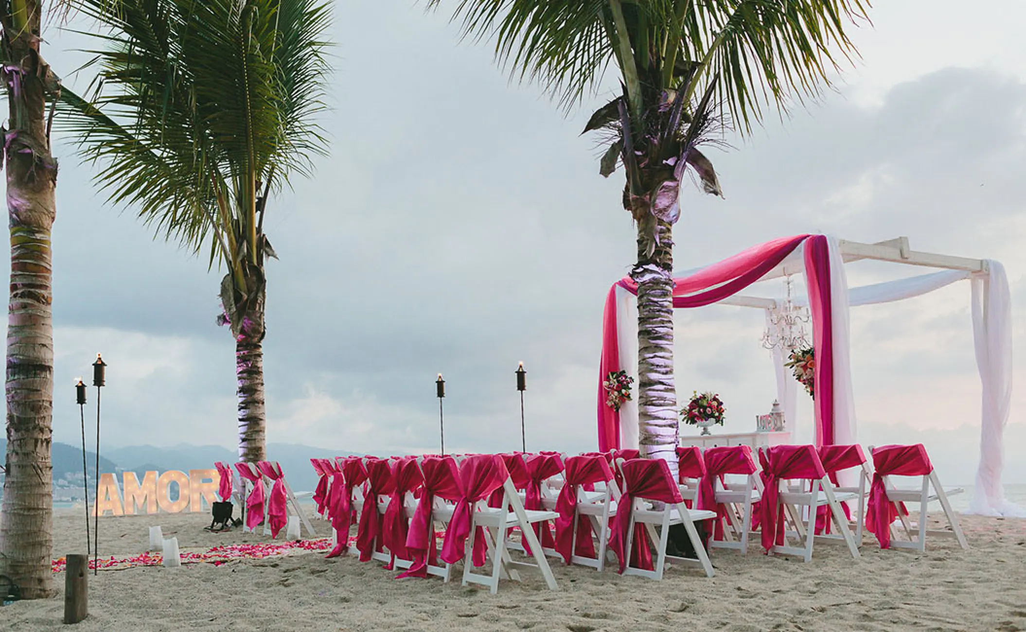Beachfront wedding ceremony with pink draped chairs and arch at Fiesta Americana Puerto Vallarta