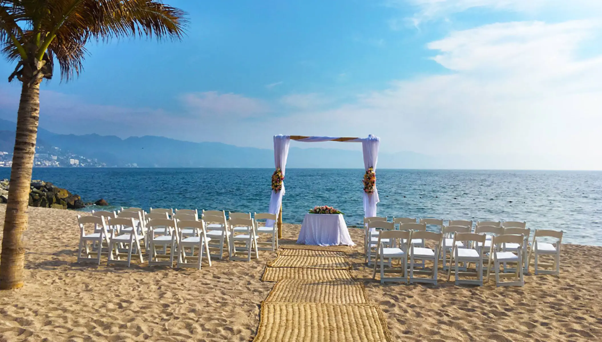 Beachfront wedding ceremony with white chairs and floral arch at Fiesta Americana Puerto Vallarta
