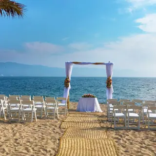 Beachfront wedding ceremony with white chairs and floral arch at Fiesta Americana Puerto Vallarta
