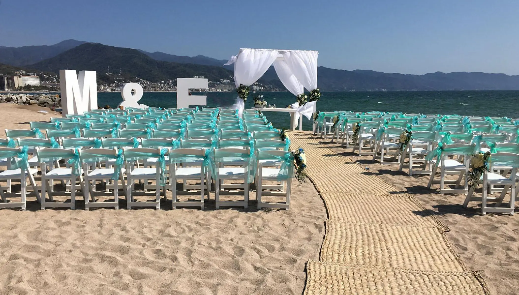 Beachfront wedding ceremony with teal-accented chairs at Fiesta Americana Puerto Vallarta