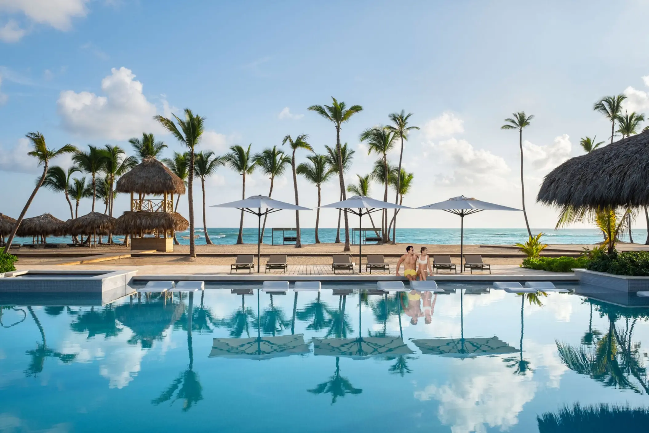 Couple sitting by the pool at Finest Punta Cana overlooking the beach and palm trees