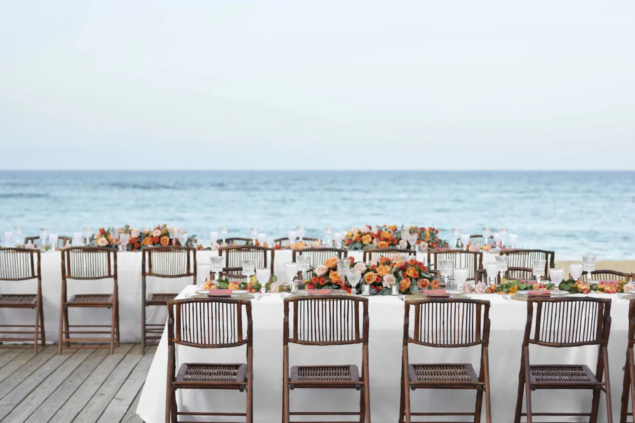 Beachfront wedding reception setup with wooden chairs and orange florals at Finest Punta Cana, Punta Cana