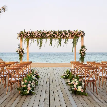Beachfront wedding ceremony with a floral wooden arch and cross-back chairs at Finest Punta Cana, Punta Cana