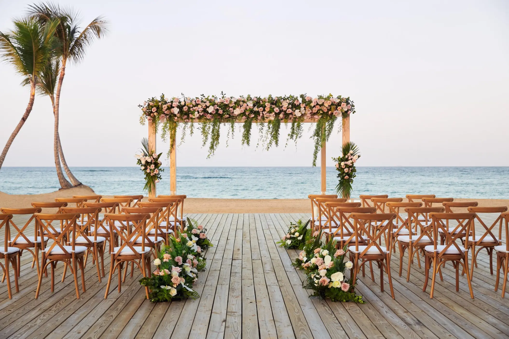 Beachfront wedding ceremony with a floral wooden arch and cross-back chairs at Finest Punta Cana, Punta Cana
