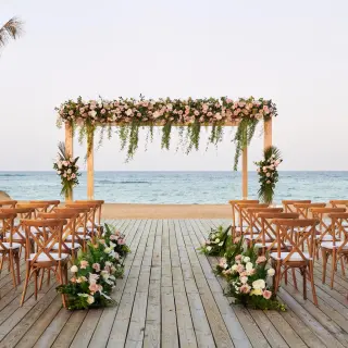 Beachfront wedding ceremony with a floral wooden arch and cross-back chairs at Finest Punta Cana, Punta Cana