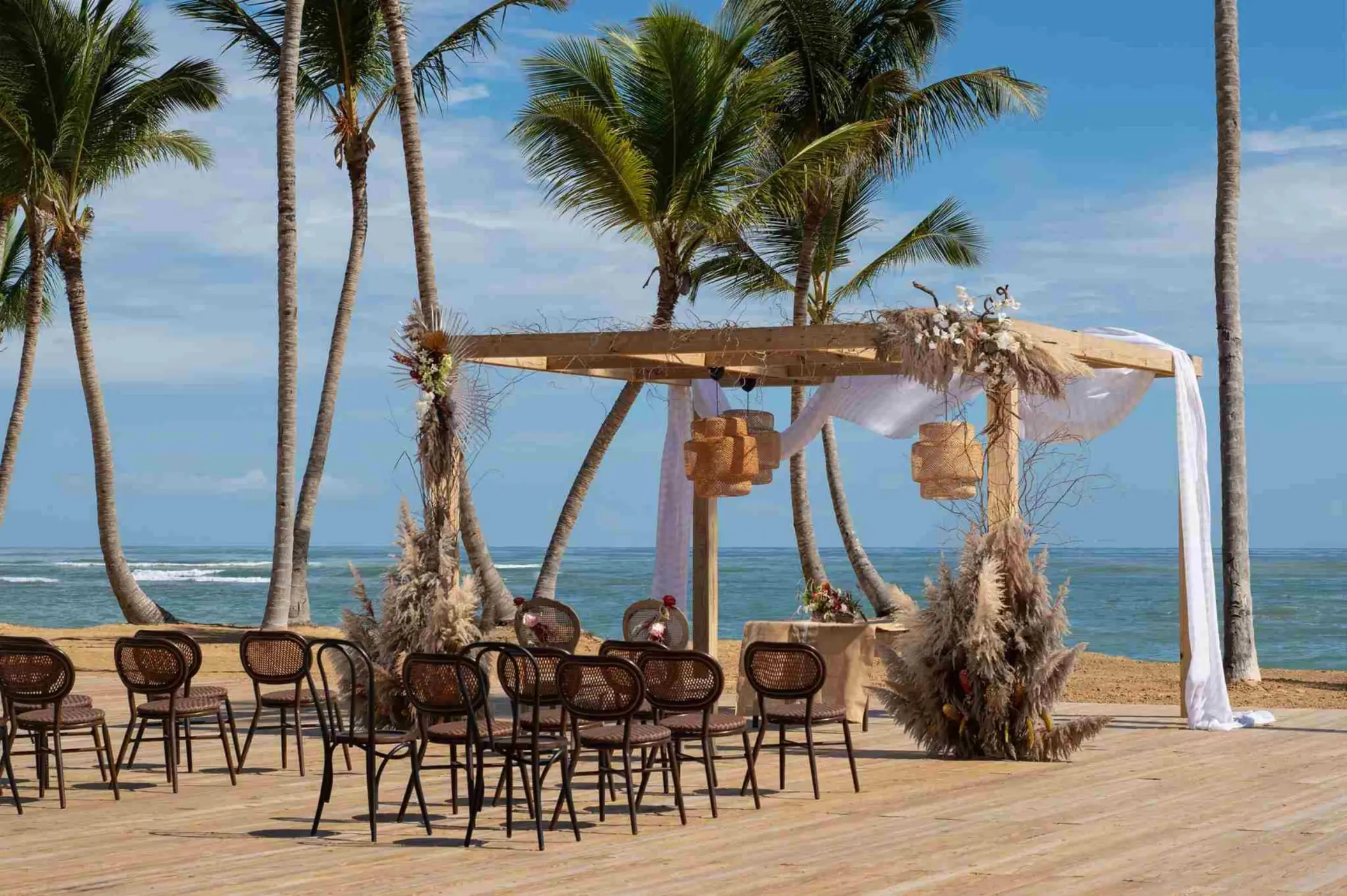 Beachfront wedding ceremony with a pampas grass arch and wooden chairs at Finest Punta Cana, Punta Cana