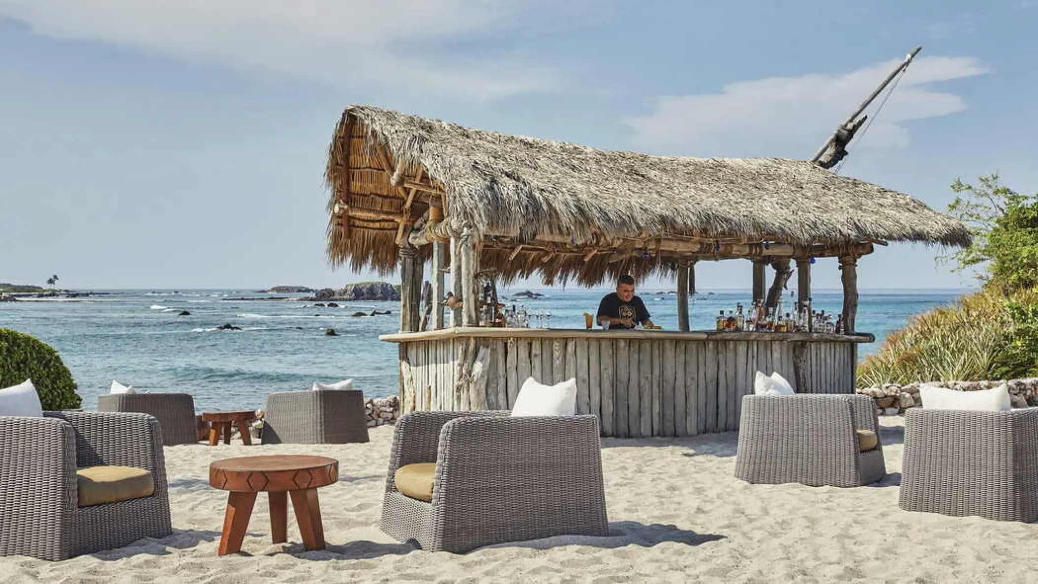 Thatched roof beach bar with wicker lounge seating at Four Seasons Resort Punta Mita