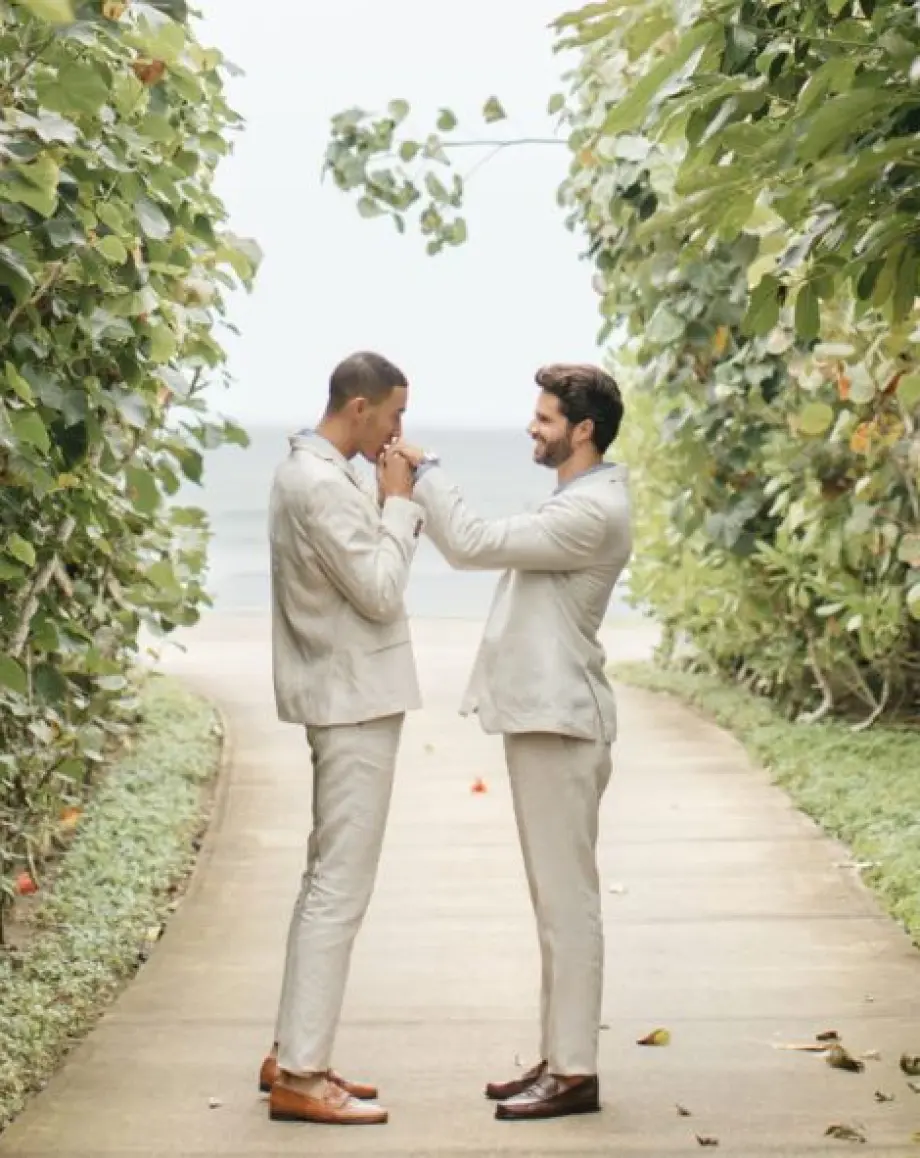 Groom kissing his partner's hand on a lush garden path at Four Seasons Punta Mita