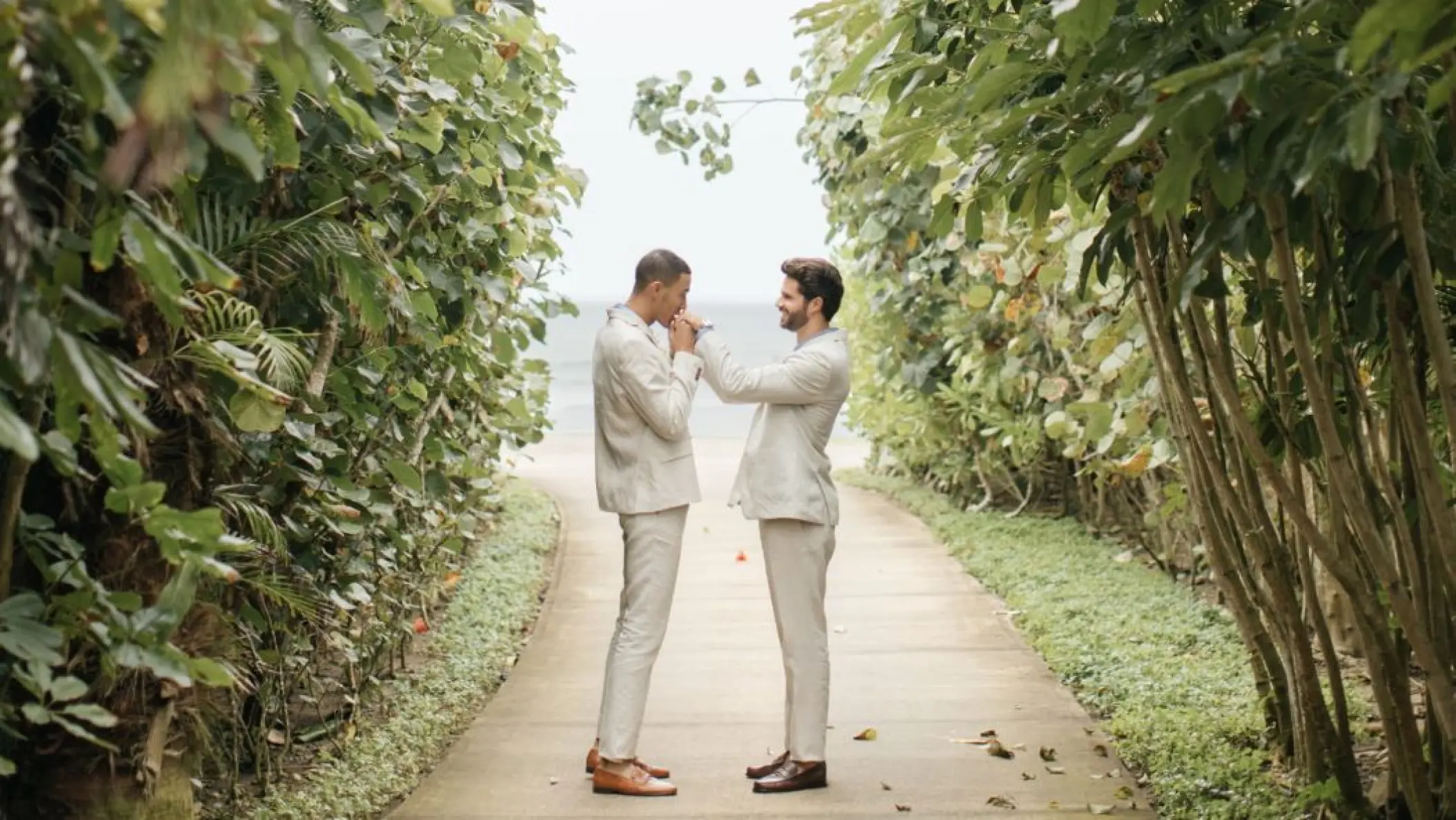 Groom kissing his partner's hand on a lush garden path at Four Seasons Punta Mita