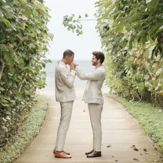 Groom kissing his partner's hand on a lush garden path at Four Seasons Punta Mita