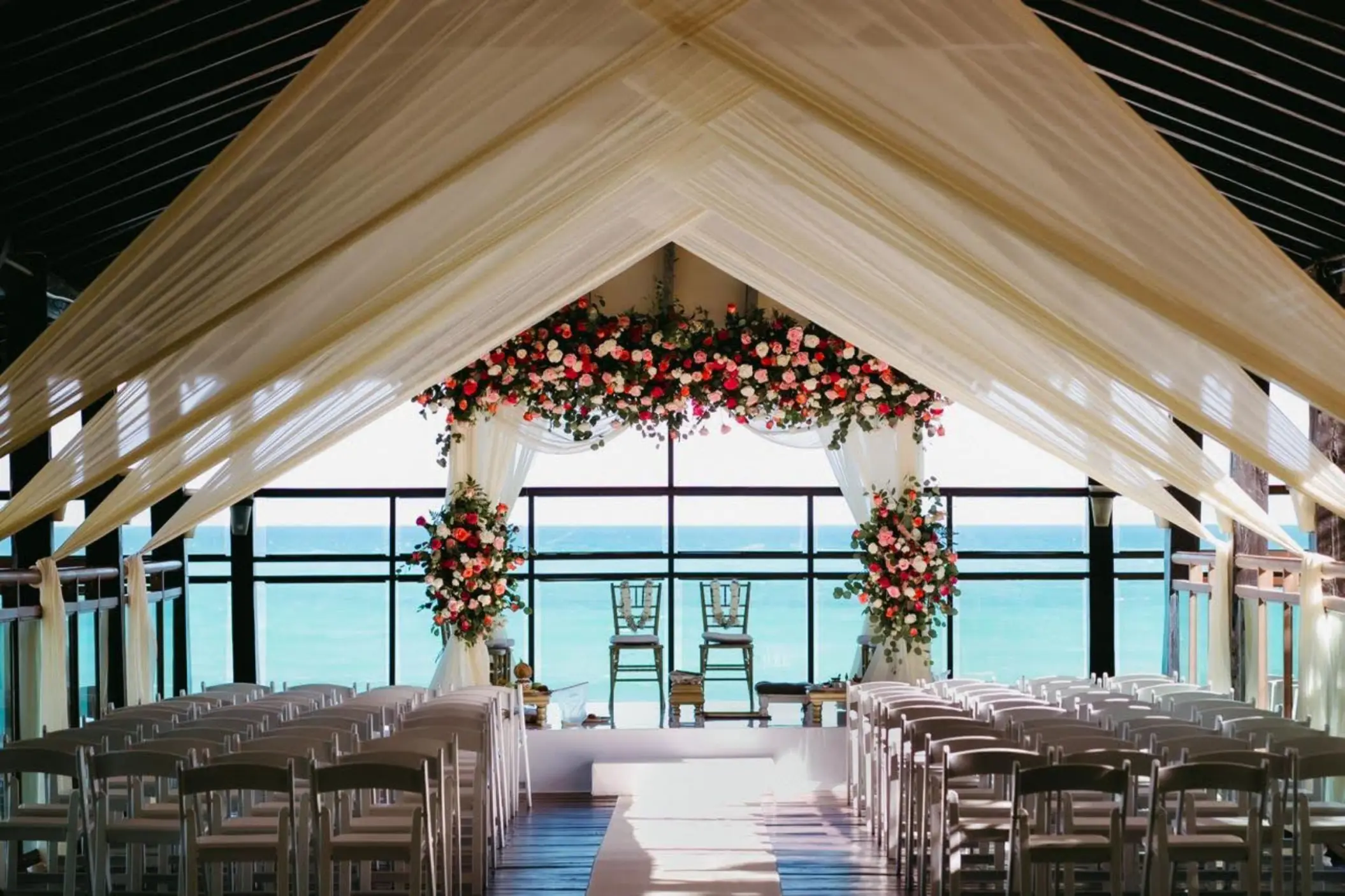 Pier deck wedding ceremony setup with white draping and red floral arch at Generations Riviera Maya, Riviera Maya