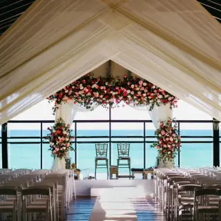 Pier deck wedding ceremony setup with white draping and red floral arch at Generations Riviera Maya, Riviera Maya