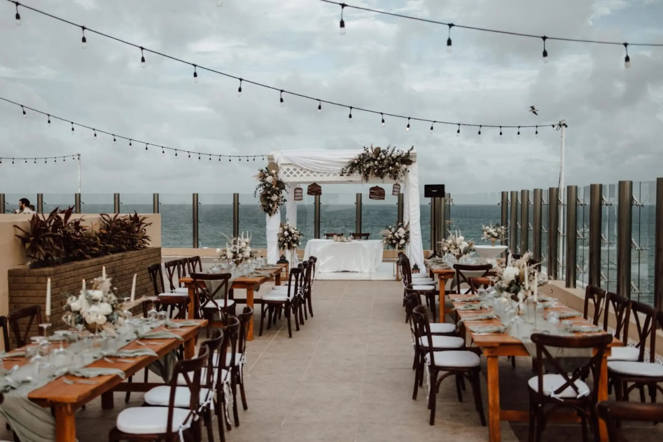 Rooftop wedding reception with long wooden tables and string lights at Generations Riviera Maya