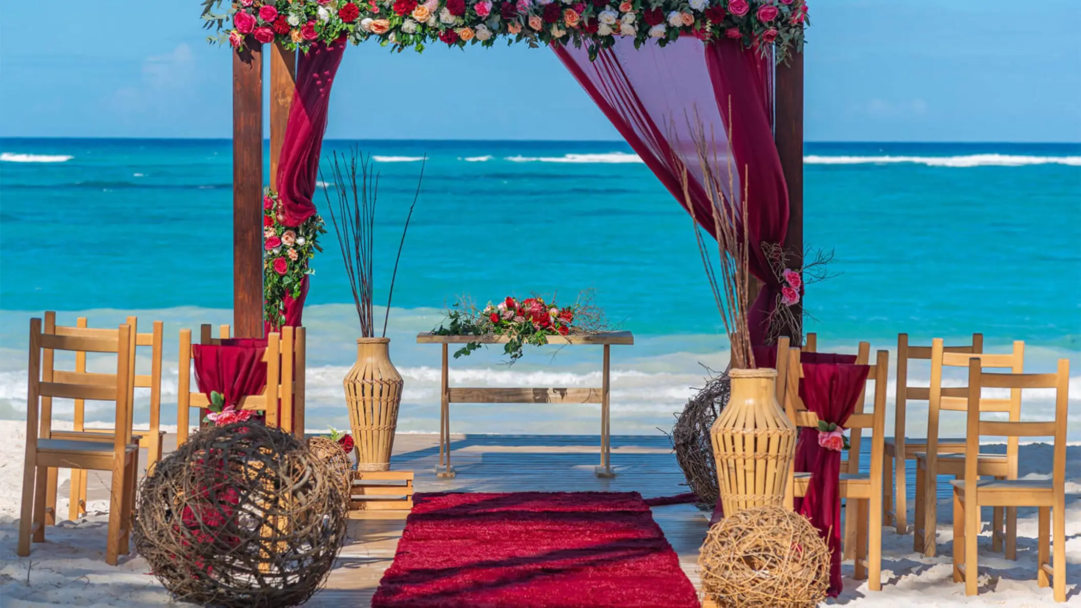 Beachfront wedding ceremony with red florals and wooden arch at Grand Bavaro Princess, Punta Cana