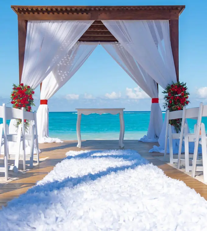 Beachfront wedding ceremony with a white draped gazebo and red flowers at Grand Bavaro Princess, Punta Cana