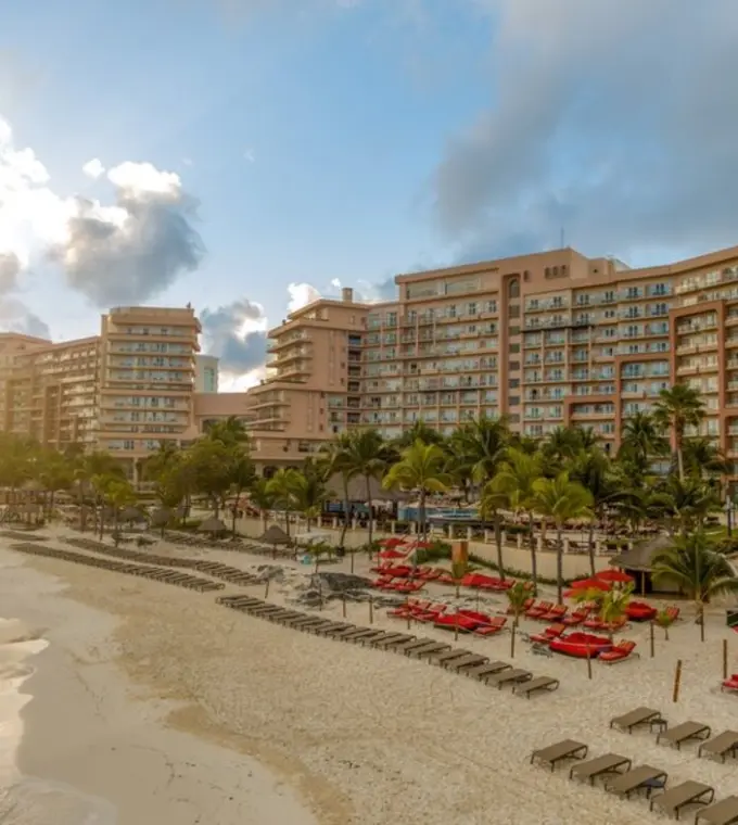 Grand Fiesta Americana Coral Beach buildings and sandy beachfront with red umbrellas at sunset, Cancun