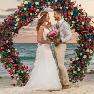 Bride and groom standing before a floral circular arch during a beach ceremony at Grand Fiesta Americana Coral Beach, Cancun