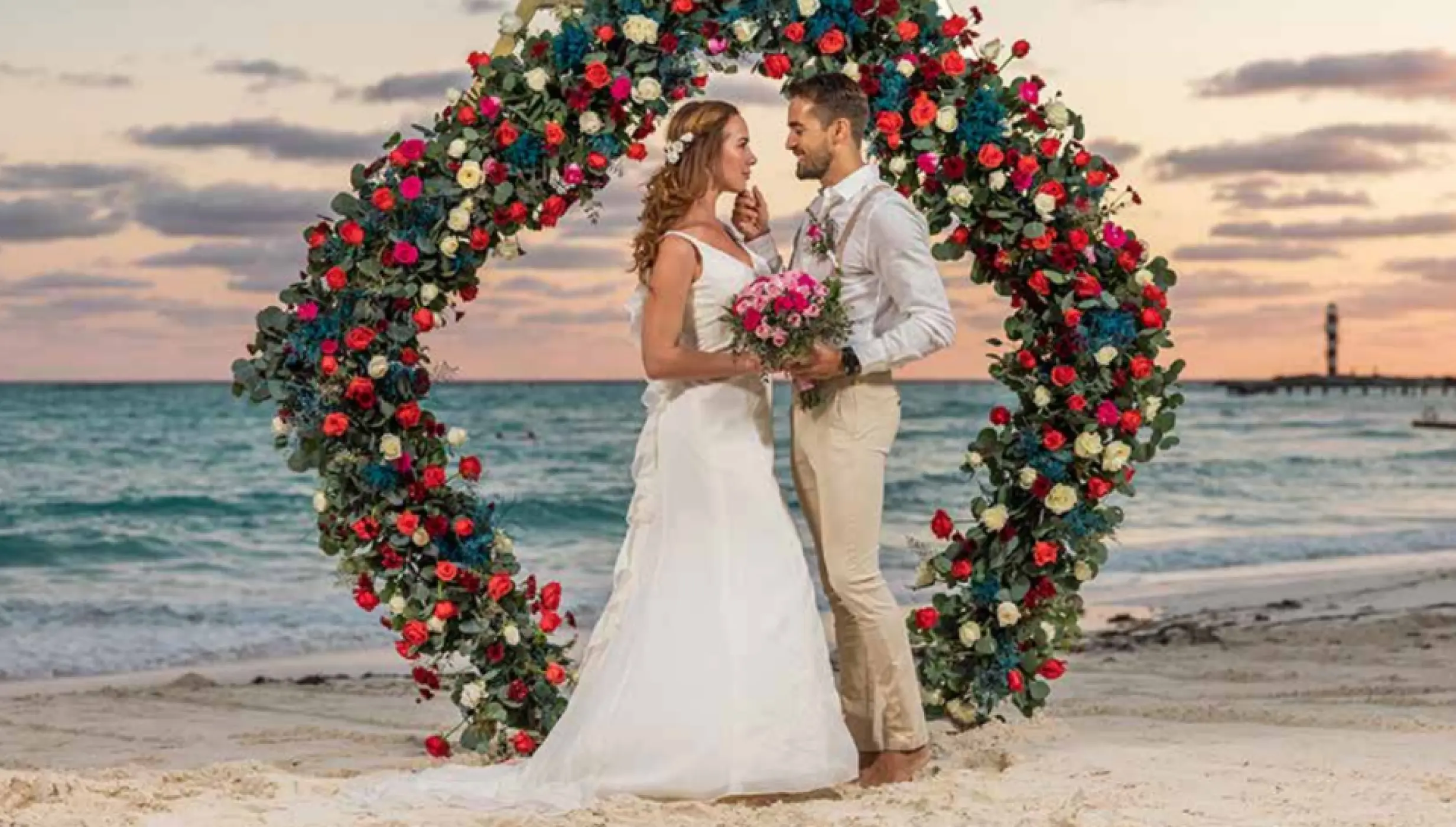 Bride and groom standing before a floral circular arch during a beach ceremony at Grand Fiesta Americana Coral Beach, Cancun