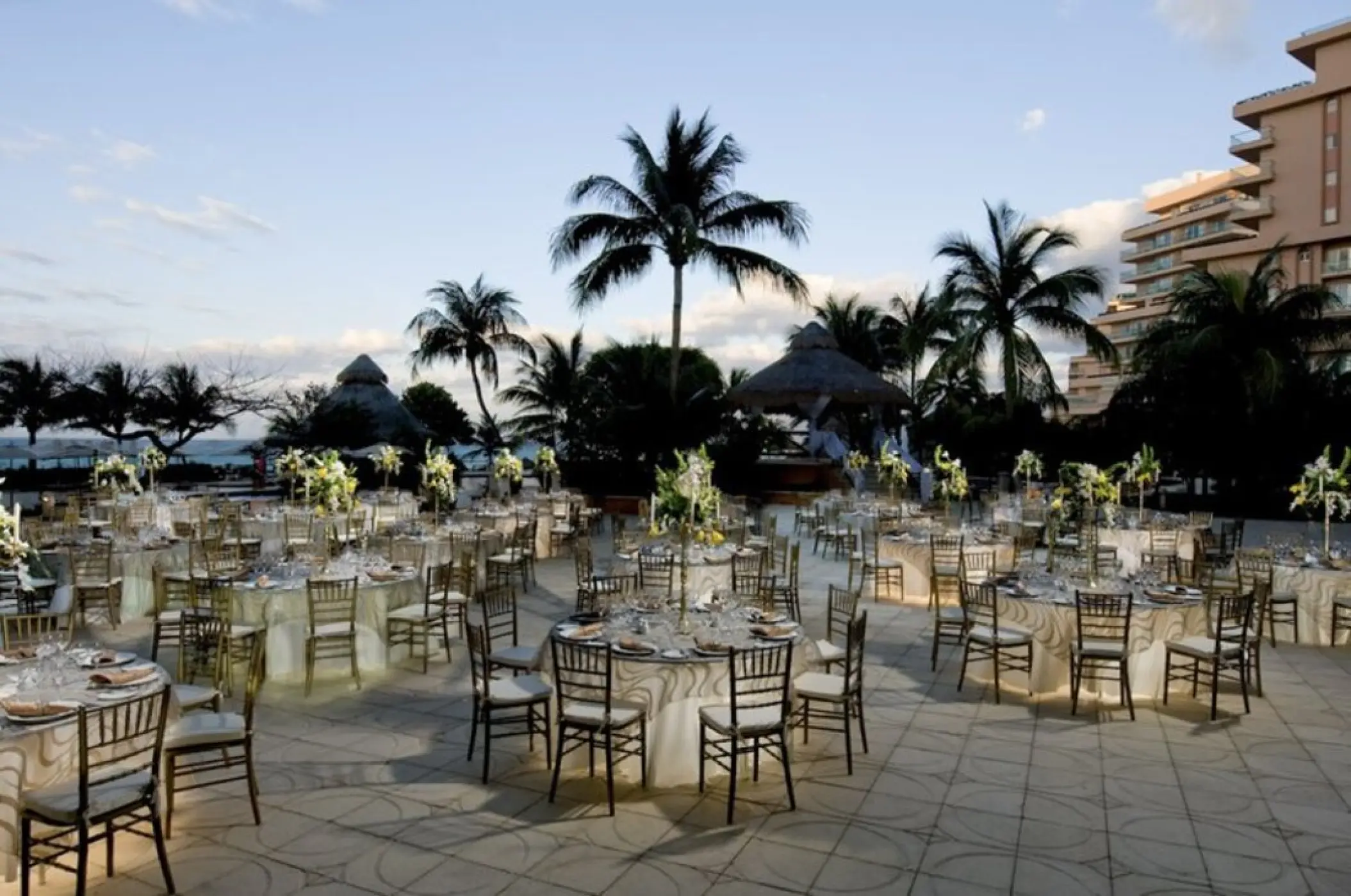 Outdoor wedding reception with round tables and gold chairs on a deck at Grand Fiesta Americana Coral Beach, Cancun