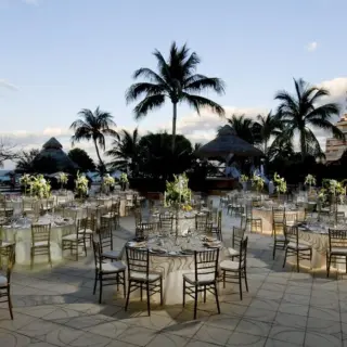 Outdoor wedding reception with round tables and gold chairs on a deck at Grand Fiesta Americana Coral Beach, Cancun